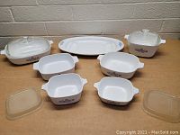 Lot of Corning Ware Blue Cornflower bakeware including covered casseroles, small casseroles, plastic lids, and serving platter on a table.