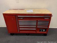 Front view of red Husky work bench showing 12 drawers, cabinet door, wood top and caster wheels