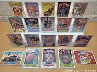 Front view of all 20 Garbage Pail Kids original trading cards displayed in protective clear sleeves, arranged in four rows on a display stand