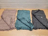 Three women's scarves laid flat on a wooden surface, showing different colors (light pink, teal, black) with polka dot pattern.