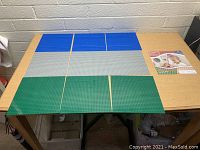 Lot of nine Lego compatible base building plates arranged on a table, showing three each of blue, grey, and green plates.