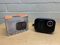 Small black ceramic desktop heater placed next to its original Soleil branded packaging box, showing front and side views.