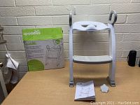 White Spuddies potty seat with ladder and two steps, accompanied by instruction manual and original box to the left.