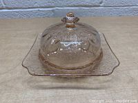 Side angle of pink glass dish showing embossed design and lid with knob