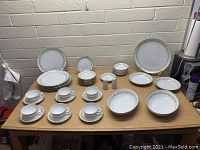 Full view of all items in the set arranged on a table showing dinner plates, bowls, cups, saucers, serving dishes, and salt and pepper shakers.