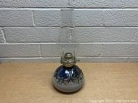 Front view of vintage stoneware hurricane oil lamp with blue and white glaze and clear chimney.