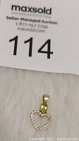 Photo showing 10K gold heart-shaped pendant with peridot and clear accent stones on a white background with auction paper.