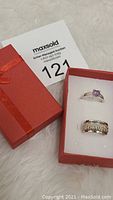 Two sterling silver rings inside a red gift box, one ring with a purple amethyst gemstone and the other a textured silver band.