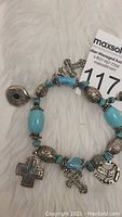 Bracelet arranged in a circle showing the turquoise beads, silver beads, and several silver charms including crosses and decorative pendants.