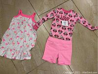 Two kids outfits laid on floor including flamingo print dress and Minnie Mouse themed long sleeve shirt with pink shorts.