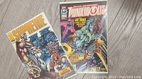 Photo showing the front covers of Supreme and Thunderbolts comic books in protective sleeves on a wood floor