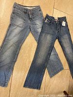 Two pairs of pants laid flat on floor showing front view. Left is light blue cotton pants, right is dark blue denim jeans.