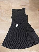 Front view of the black sleeveless dress with small white dots, laid flat on a beige tiled floor.