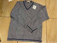 Blue and white speckled cotton V-neck sweater with navy blue trim on neckline, sleeve cuffs, and hem, size 16 (M), laid flat on a beige tile surface.