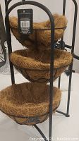 Close-up view of the three woven natural fiber baskets secured in black metal circular frames as part of the tiered plant stand.