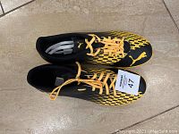 Top view of the black and yellow Puma soccer shoes showing the size 47 tag on right shoe.