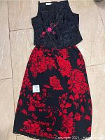 Photo of the full two-piece outfit laid flat, showing black sleeveless top with pink floral embroidery and black skirt with red floral print.