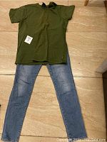 Photo of a women's outfit consisting of light blue size 12 denim pants and a medium-sized green t-shirt laid flat on the floor.