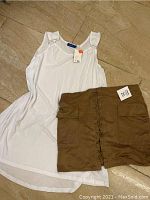 White sleeveless Apt. 19 shirt laid out flat next to brown skirt.