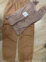 Tan pants with elastic waist and multiple pockets, paired with a sleeveless light brown shirt featuring lace detail on straps and chest.