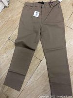 Full view of taupe Amanda pants laid flat on tiled floor showing front side with tag attached.