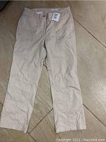 Image of one pair of beige size 10 pants laid flat showing front side and button closure with a size tag 28 visible.