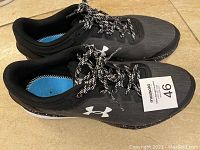 Pair of black Under Armour athletic shoes side view with maxsold size tag 46 visible on left shoe.