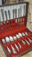 Full open wood box showing silver plated knives, forks, spoons, and teaspoons organized in rows with red velvet interior.