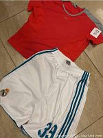 Full view of the red Nike shirt and white Adidas Real Madrid shorts on tile floor.