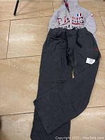 Full view of the sports outfit laid out on the floor, showing gray Puma pants with France jacket behind.