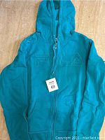 Front view of teal Fila hoodie jacket with zipper and kangaroo pockets.