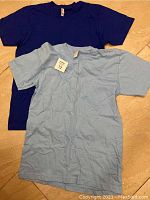 Both T-shirts laid out on a surface, showing colors and size tags.