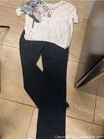 Full outfit laid flat on tile floor, showing black pants and white floral blouse