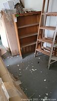 Wooden bookcase standing in a garage or storage area with various items nearby.