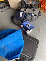 Camera bags piled with a boxed Canon Powershot S215 digital camera and other gear visible on gray concrete floor.