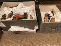 Various hand carved wood figural sculptures grouped in two storage boxes with tissue paper