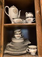 All pieces arranged inside a cabinet showing full service plus coffee pot, sugar bowl and creamer
