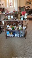 Front view of wooden display shelf unit holding various glassware and decorative items, showing the spindle leg design and shelf layout.