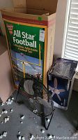 Photo of boxed All Star Adjustable Football Goal Post with a black floor fan and boxed ceiling fan light fixture beside it.