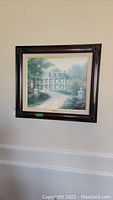 Framed artwork by Thomas Kinkade hanging on a beige wall, showing the entire piece including the frame.