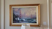 Framed artwork of Golden Gate Bridge with waves and boats, gold frame with white matting