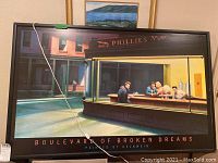 Front view of the framed lighted art print showing four figures inside a diner with a street exterior. The lighting strip power cord is visible.