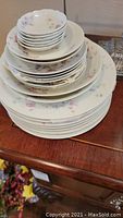 Stacked collection of Limoges porcelain plates and bowls with delicate pink and purple floral pattern and gold rim accents.