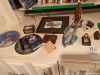 Front of various memorabilia pieces including plates, watch, vase, figurines arranged on a shelf.