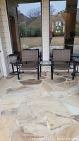 Two brown vinyl weave outdoor chairs with black metal frames positioned on stone patio in front of glass doors.