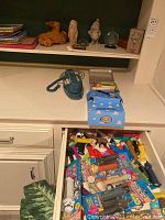 Wide view of lot showing carved stone dwarfs, wooden car, vintage blue rotary phone, Toy Story lunch box on shelf, drawer open showing many loose Pez dispensers.