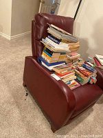 Maroon leather recliner chair with a stack of books on the seat showing the front and side profile.