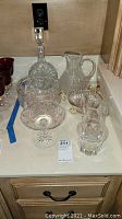 Six Waterford crystal pieces displayed on a counter including a decanter, pitcher, covered jar, and bowls.