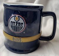 Lower side view of a navy ceramic mug with Edmonton Oilers logo and gold band with team name.