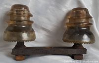 Pair of mounted amber glass insulators on rusted iron metal base with bolts, showing some wear and discoloration.